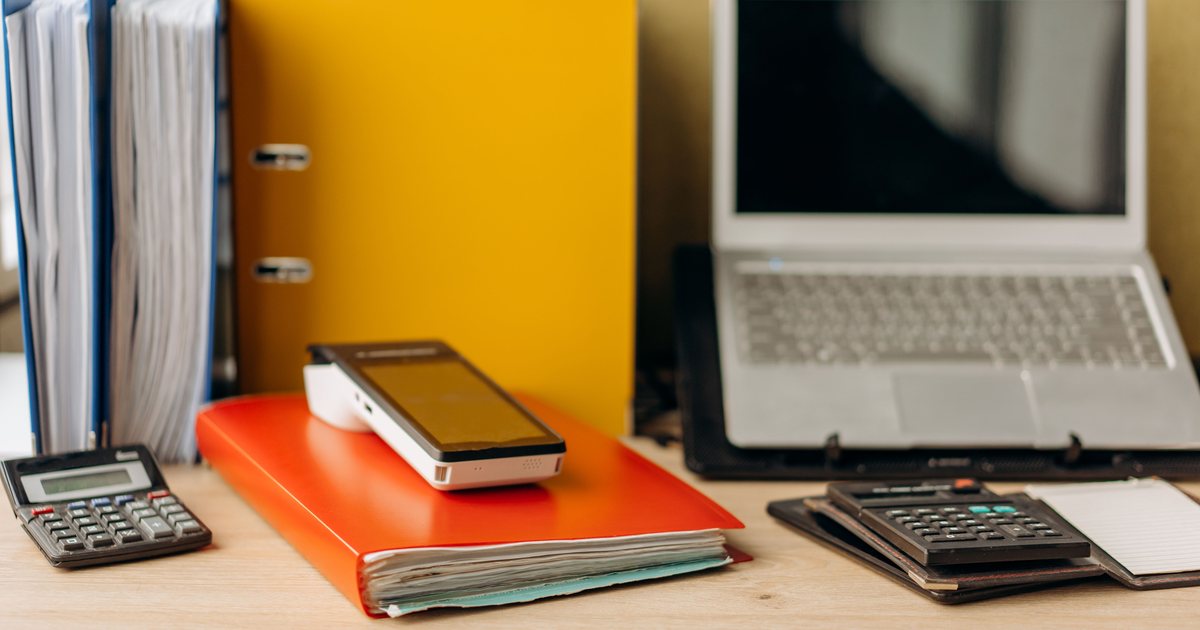 Mesa de oficina con portátil, calculadoras, carpetas de documentos y un teléfono móvil