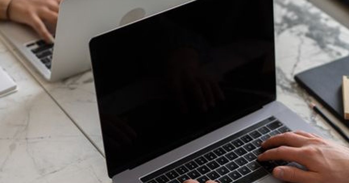 Manos escribiendo en el teclado de un portátil sobre una mesa de mármol