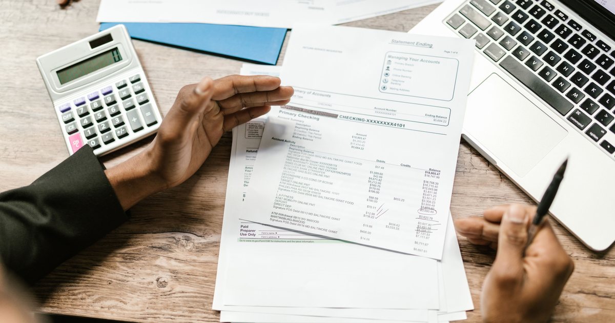 Manos sosteniendo una factura de proveedor junto a una calculadora y un portátil