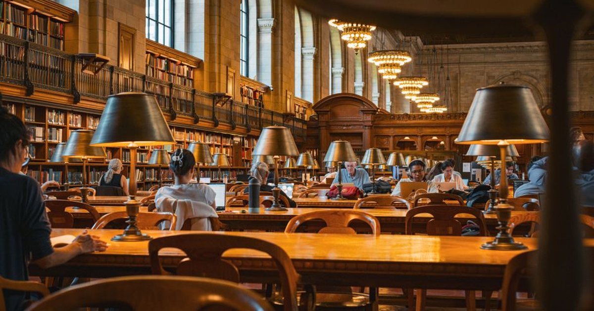 Sala de lectura de una biblioteca vacía con hileras de mesas y lámparas