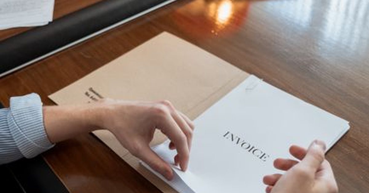 Manos sobre una carpeta de facturas con la palabra INVOICE en un escritorio de madera