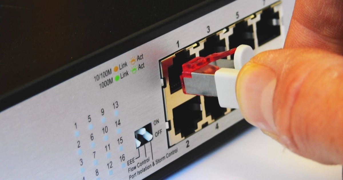 Mano conectando un cable de red a un conmutador de red, en primer plano