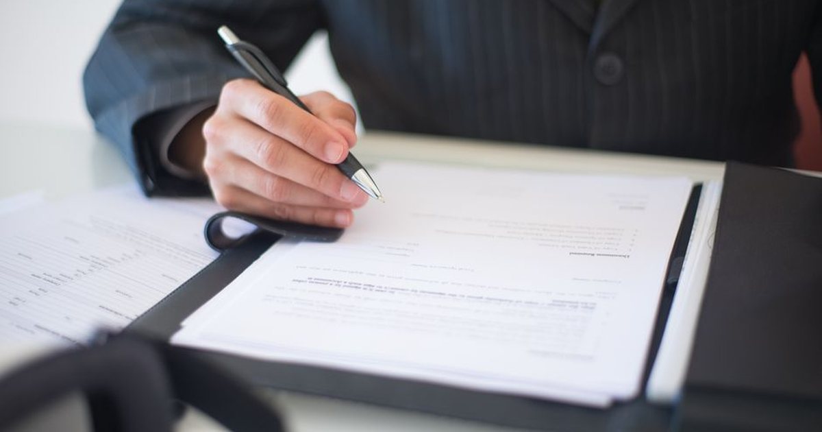 Persona firmando un documento con traje de oficina, sin mostrar el rostro