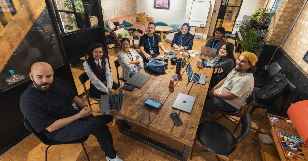 Equipo diverso de ocho personas reunido alrededor de una mesa con portátiles