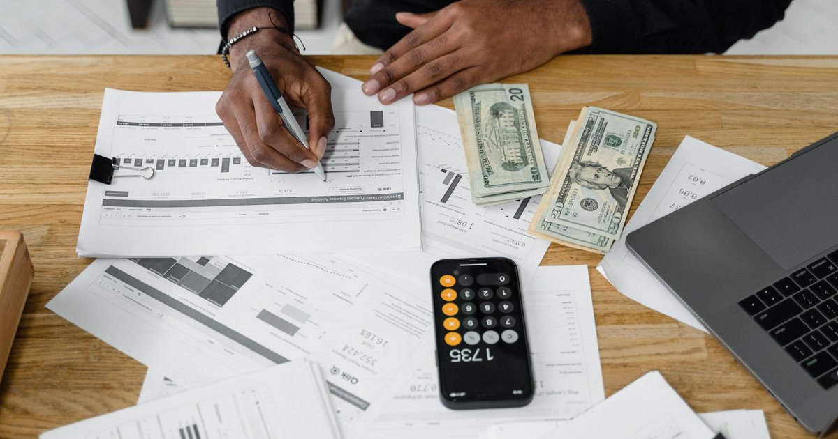 Persona anotando cifras sobre facturas y gráficos en papel junto a una calculadora y un portátil