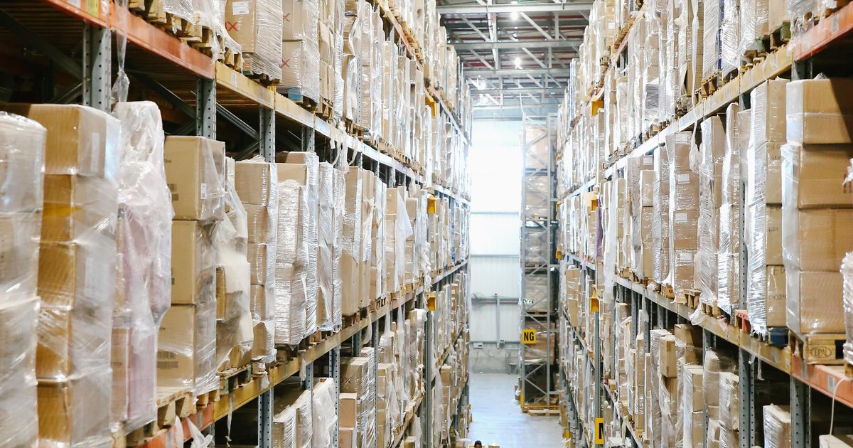 Pasillo de un almacén logístico con estanterías llenas de cajas envueltas en plástico