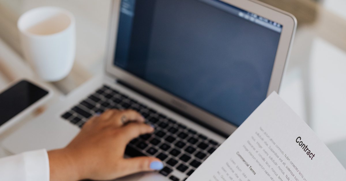 Manos escribiendo en un portátil junto a documentos impresos