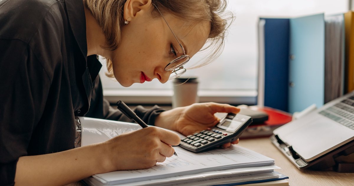 Persona trabajando con una calculadora y documentos contables junto a una pila de archivadores