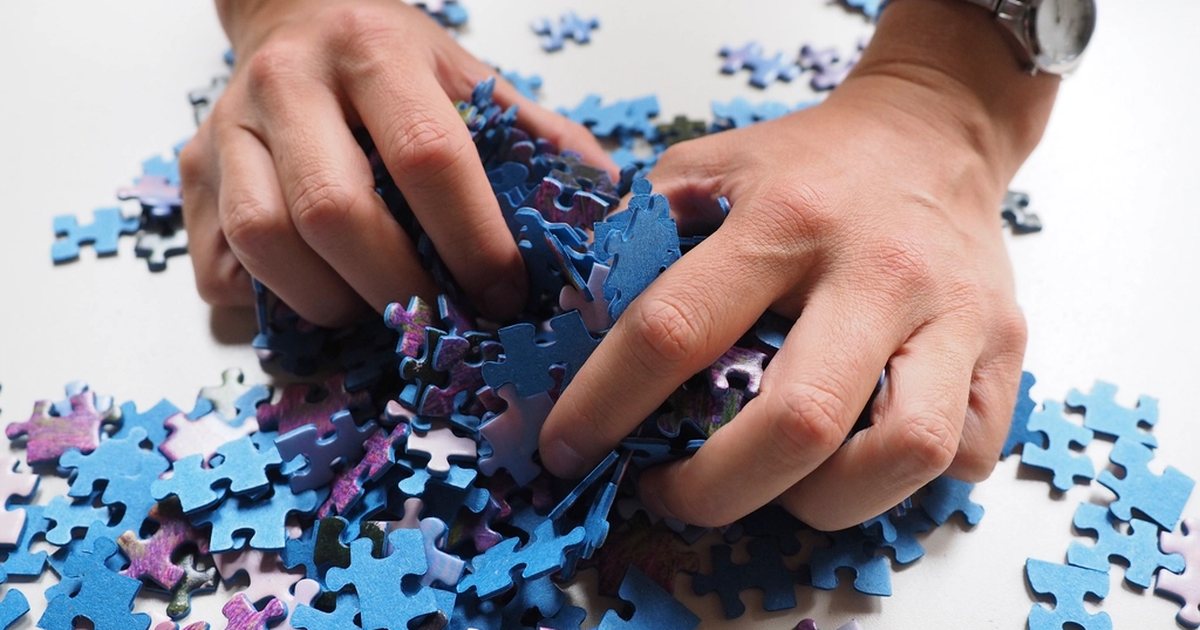 Manos juntando piezas de puzzle de colores sobre una superficie clara