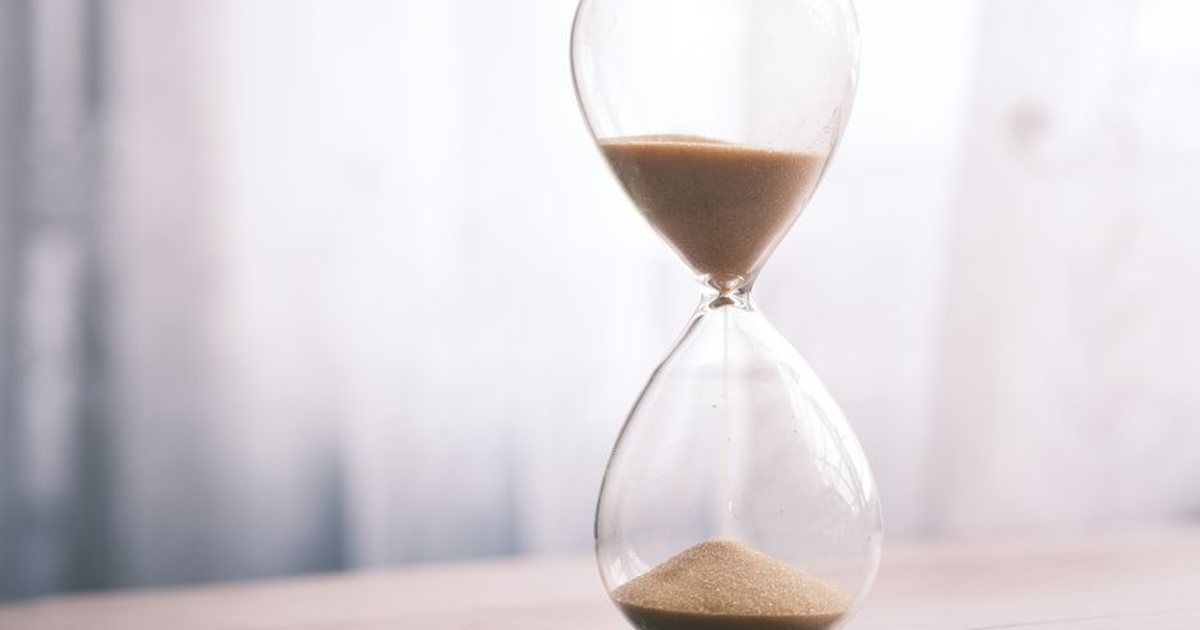 Reloj de arena con arena cayendo, sobre una superficie de madera