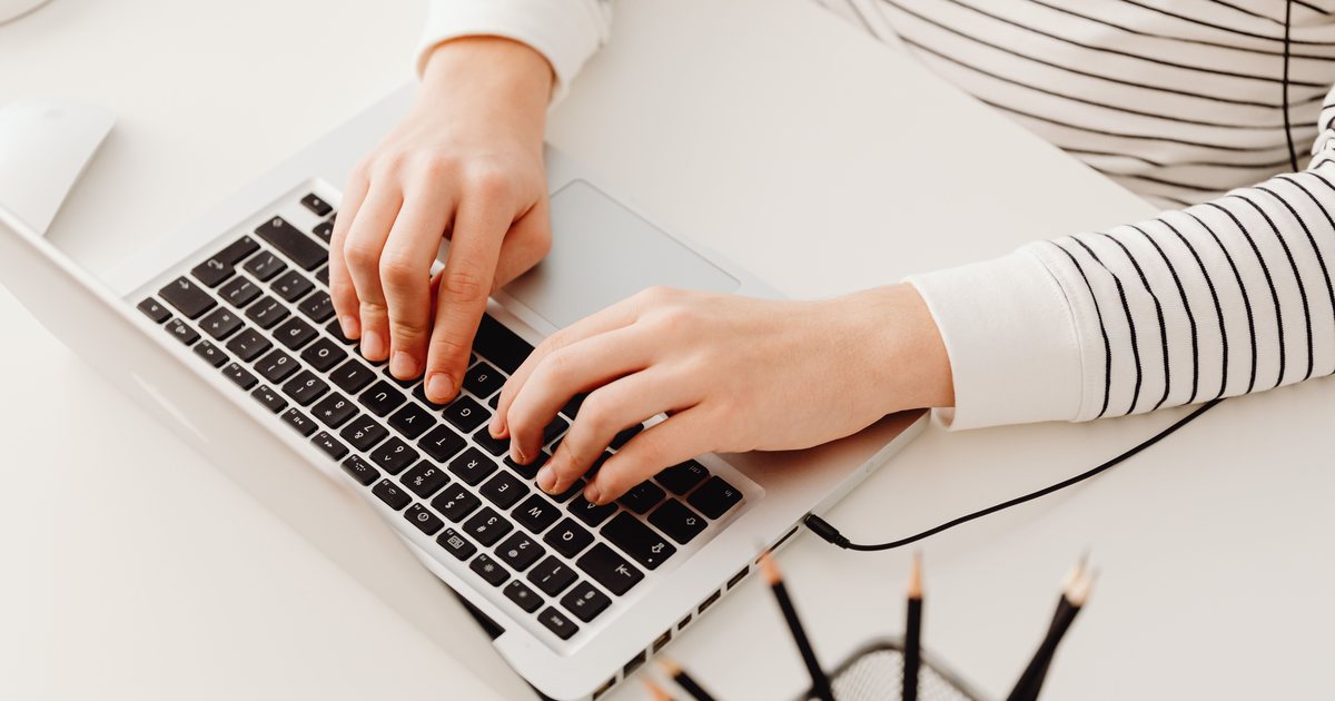 Manos escribiendo en el teclado de un portátil sobre una mesa de oficina