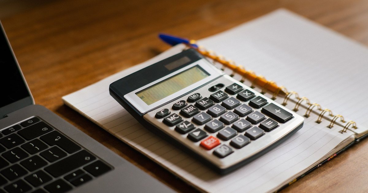 Calculadora sobre un cuaderno junto a un portátil en una mesa de madera