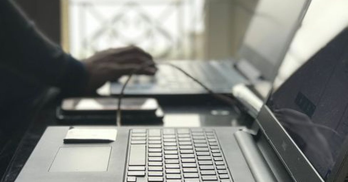 Manos escribiendo en un portátil junto a una ventana con celosía