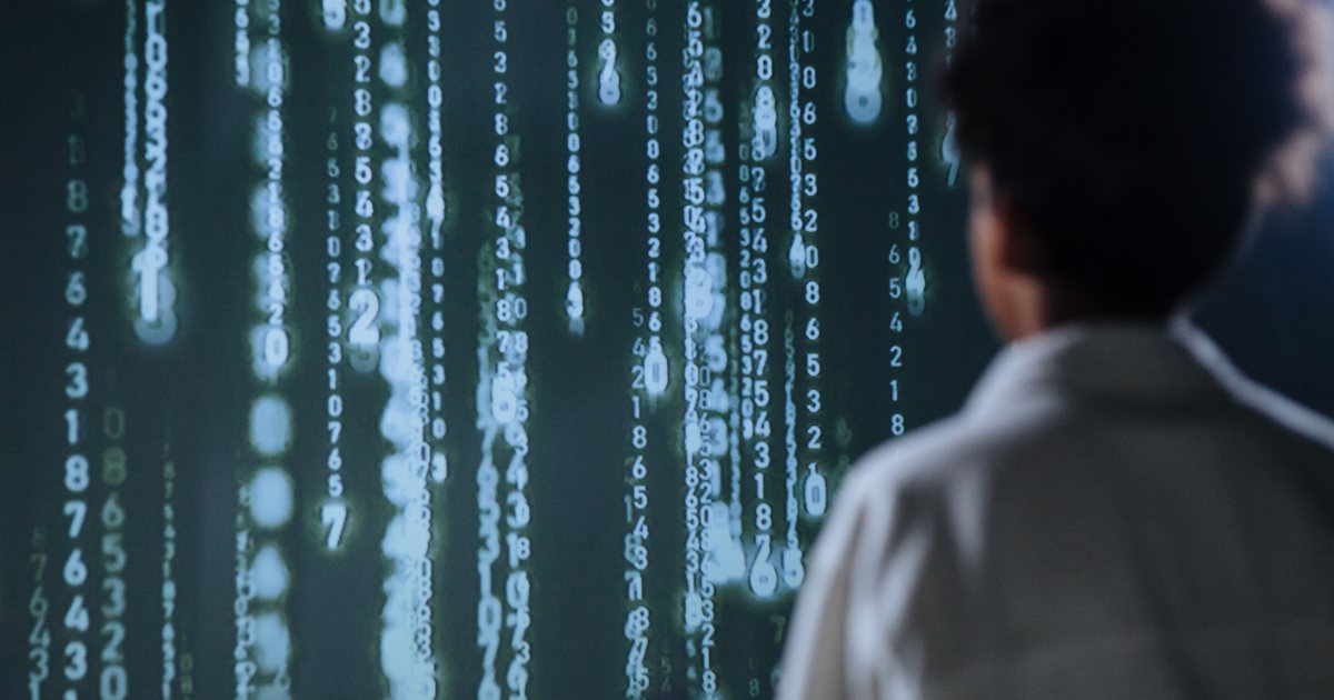 Persona de espaldas observando una pantalla con columnas de datos numéricos en movimiento