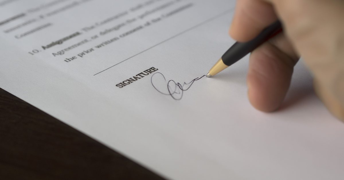 Mano firmando un contrato con bolígrafo sobre una mesa de madera