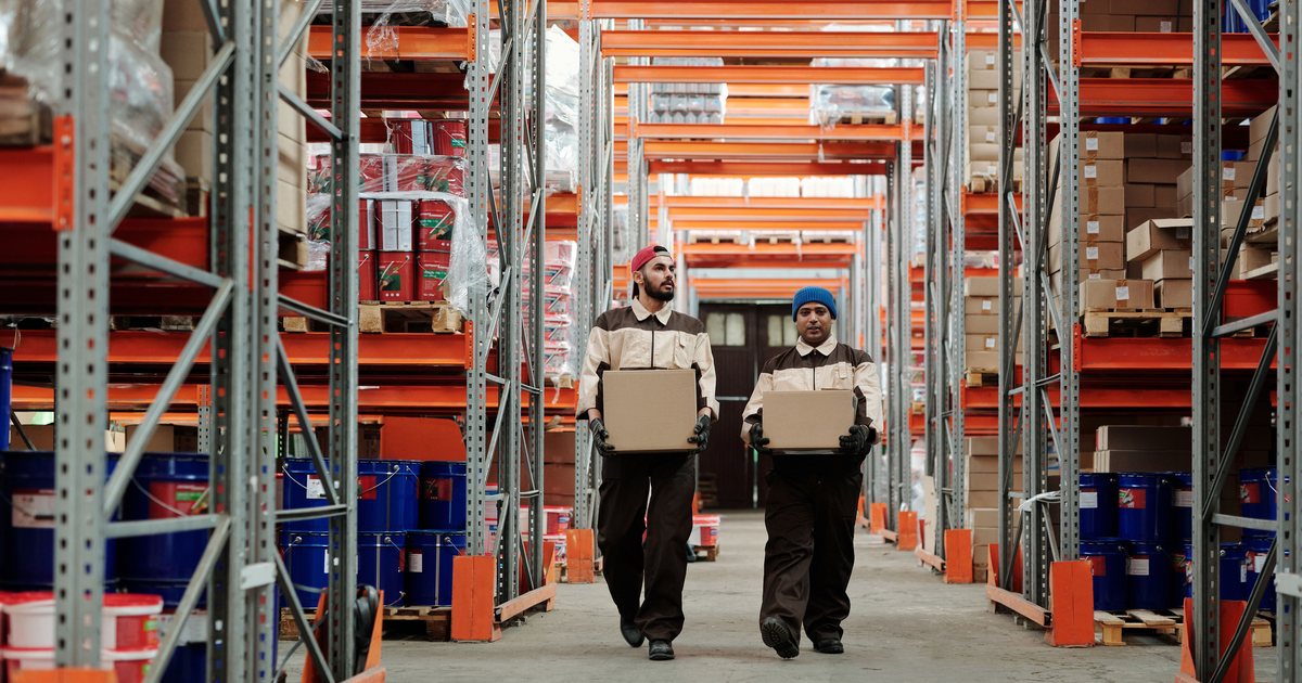 Dos operarios de almacén transportando cajas entre estanterías industriales