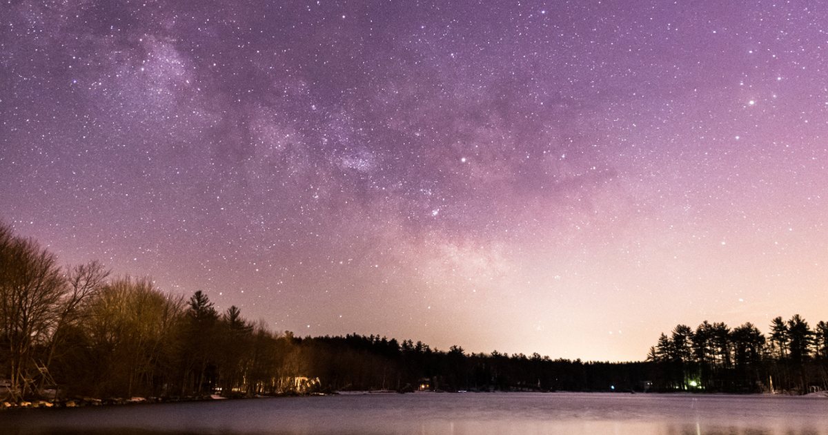 Cielo estrellado reflejado en un lago con tonos morados y rosados durante la noche